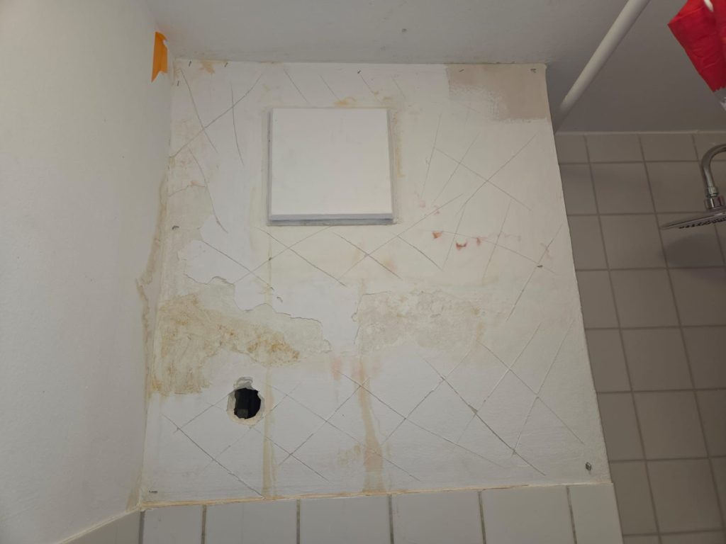 Wasserschaden im Sanitärbereich vor der Sanierung mit sichtbaren Feuchtigkeitsspuren an der Wand